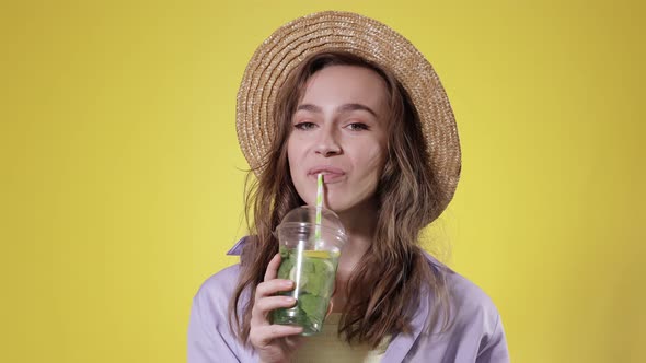 Surprised Woman Drink Mojito cocktail From Plastic Cup Over Yellow Studio Background alt