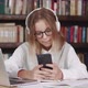 Surprised Young Teen Girl with Glasses Sit of the Table at Library Holding Phone Looking at Screen