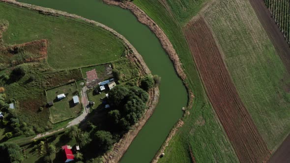 Aerial top down shot of a calm curvy river among the fields and farms of a small village. alt