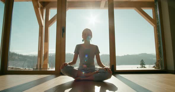 Meditating Woman in Pajamas Sits in Lotus Pose By Big Window in Morning at Home alt