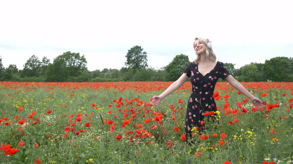 Blonde girl in headphones in poppies field in summer time