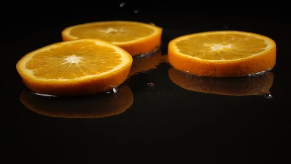 Orange Slices Fall on the Black Surface Covered with Water alt