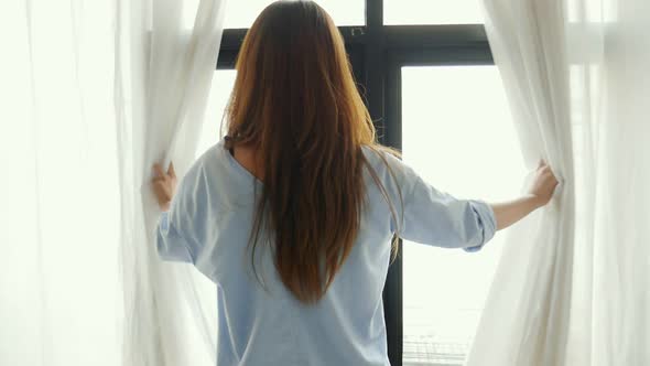 A young Asian woman opens the curtain and stretches Beside the window.