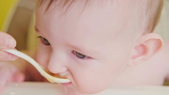 Mom feeding toddler baby from a spoon on a high chair for children, studio yellow background. alt