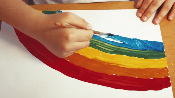 A Child's Hand Draws a Beautiful Rainbow with Colored Paints on a Sheet alt