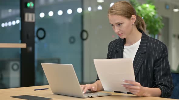 Beautiful Young Businesswoman Working on Laptop and Paperwork in Office alt