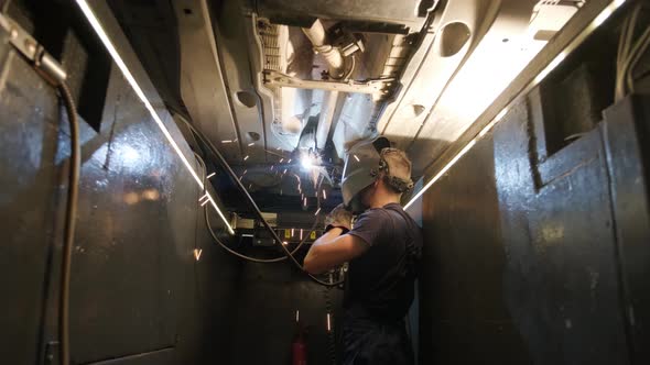 Car service worker welds and repairs an exhaust pipe of a car. Close-up welding 