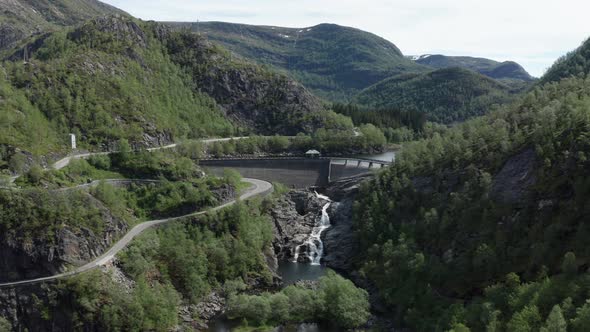 Aerial ascending shot over Dam with winding roads on valley of Norwegian Mountains alt