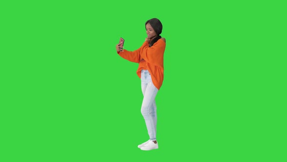 Smiling African American Woman in Bright Jumper Taking Selfie and Checking Her Phone on a Green alt