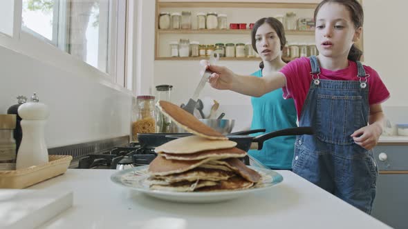 Two young girls preparing pancakes in the kitchen using a frying pan alt
