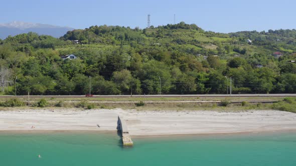 Red Car Drive Along Grey Asphalt Road Between Hills and Sea alt
