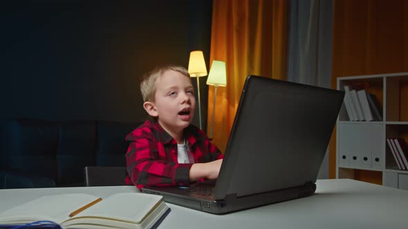 Cute Preschool Boy HomeschooledSitting Behind a White Table Doing His Homework on the Laptop alt