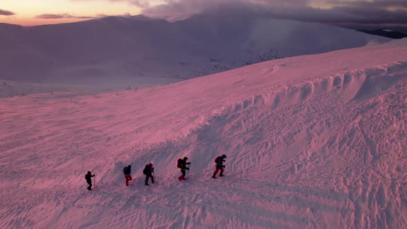 Aerial Flight Above Group of People Hiking on Snow Covered Mountain During Pink Sunset.
