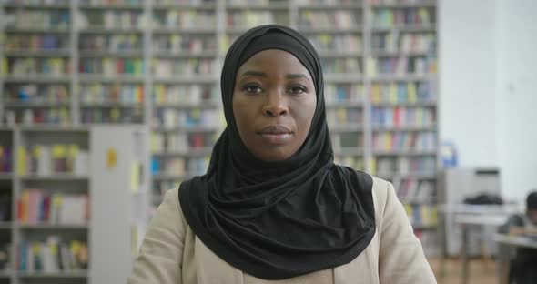 Muslim Woman in Black Hijab Looks in Camera Sitting at Desk alt