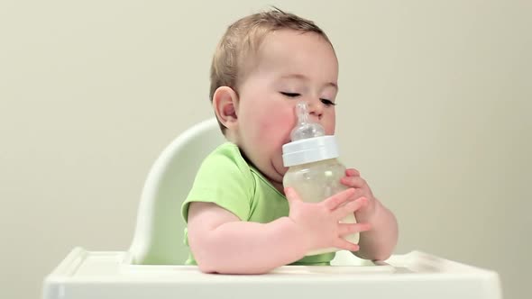 Baby boy sitting in highchair with bottle of milk alt