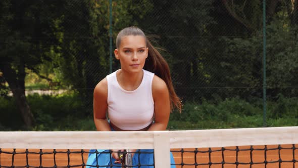 Young woman walking through tennis court with racket. Attractive brunette female entering tennis har