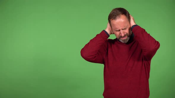 A Middleaged Handsome Caucasian Man Hears a Loud Noise and Covers His Ears  Green Screen