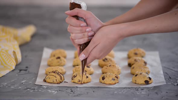 Female chef decorating pumpkin cookies with melted chocolate.