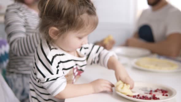 Funny Little Girl is Licking the Condensed Milk From the Pancake While Mother Feeds the Cat alt