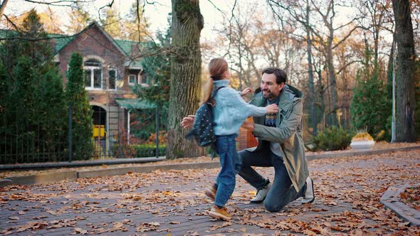 Little Daughter Schoolgirl Running Up to Smiling Father Hugging and Talking to Him alt