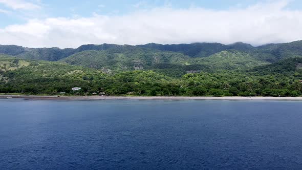 Flying towards a rugged, remote and secluded mountainous volcanic tropical island covered in trees, alt