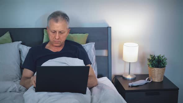 A Middleaged Man Works Online on a Laptop While Lying in Bed at Home Late at Night