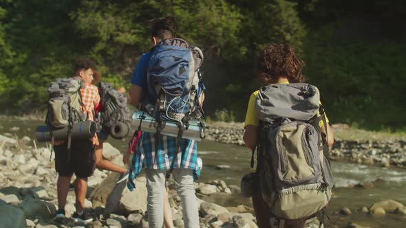 Rear View of Diverse Multiracial Tourists with Backpacks Backpacking By Mountain River alt