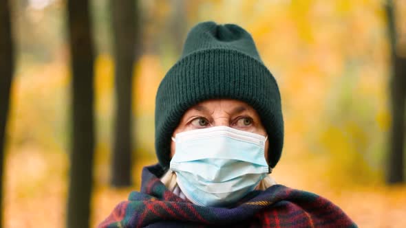 An Elderly Woman 50s Wearing Warm Clothes and a Protective Medical Mask Looks at the Camera alt