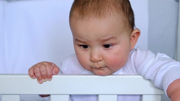 Cute portrait of a baby in a crib close-up. A child in white clothes on white underwear. Tenderness alt