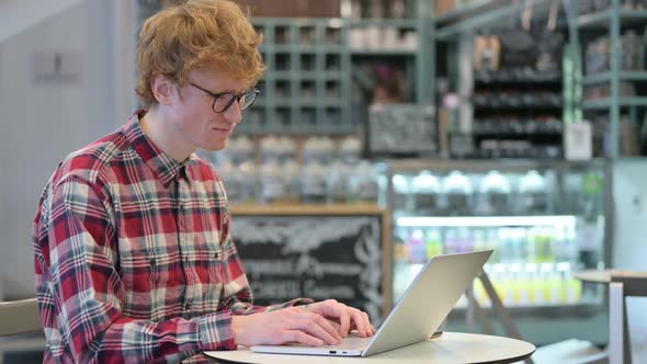 Young Redhead Man Reacting to Loss on Laptop in Cafe alt