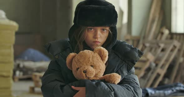 Portrait of a Homeless Girl with Grey Eyes Wearing Hat with Earflaps Looking at the Camera alt
