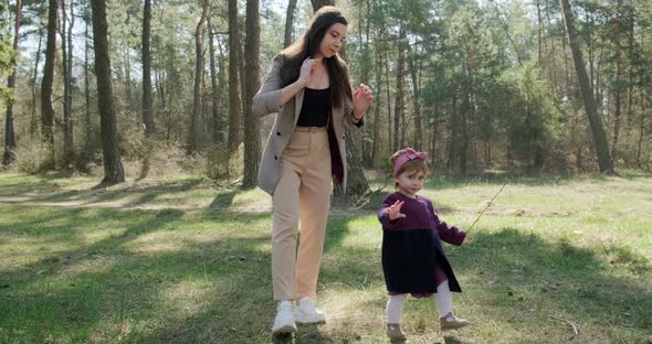 Happy Little Girl Walking and Playing with Mother Among Trees in Coniferous Forest. Healthy Child