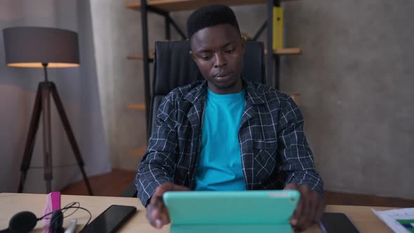 Front View of Busy Concentrated African American Young Man Scrolling Tablet Screen Surfing Internet alt