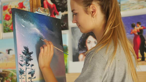 Smiling female artist paints picture on canvas with oil paints