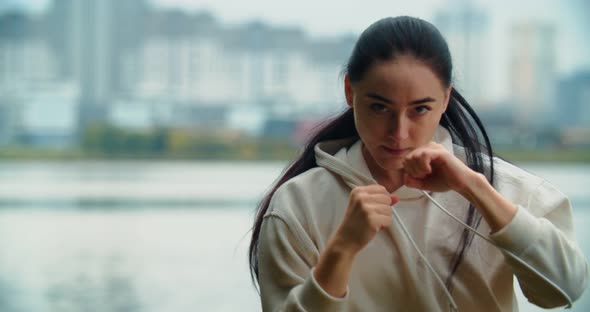 Young girl in boxing gloves and sport clothes is boxing while training by seaside, near the city