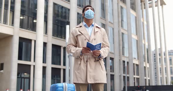 Man in Safety Mask Holding Vaccination Certificate for Covid19 Standing with Suitcase Outdoors alt