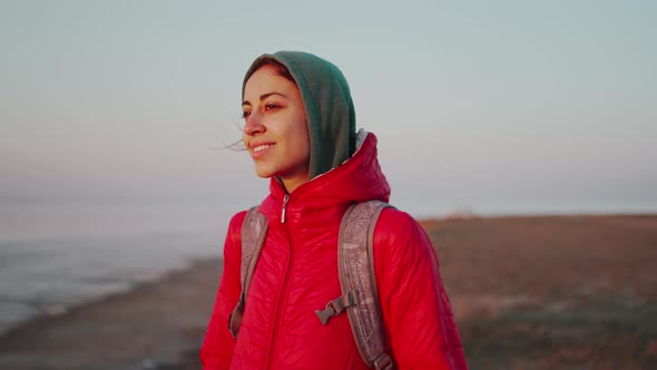 Young Woman Traveler with Backpack Meeting Sunrise at Deserted Sea Beach alt