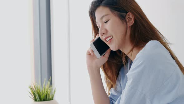 Beautiful young woman Asian calls phone beside the window in the bedroom at home.