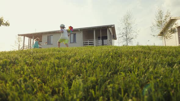 Happy Little Kids Running on Green Lawn and Holding Colored Windmill Toy alt