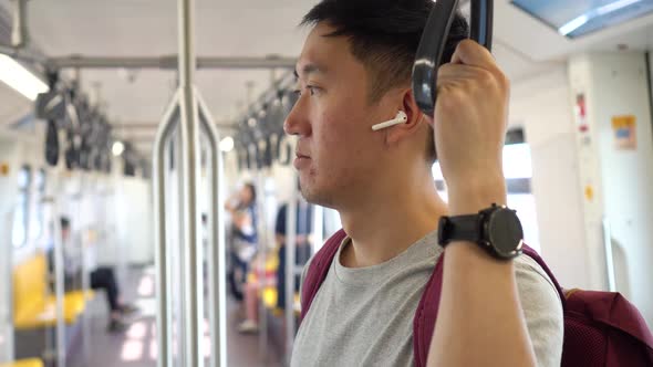 Close Up of Young Man Listening to Music with Wireless Earpods While Commuting By Train alt