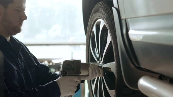 Auto Mechanic Tightens the Nuts on the Wheel of a Car