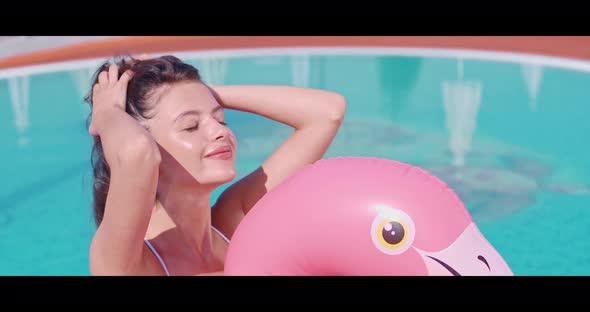 Positive Woman Swimming on Inflatable Flamingo in Pool alt