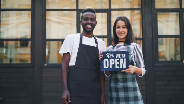 Slow Motion Portrait of Man and Woman Business Partners Holding Cafe Open Sign and Smiling Looking alt