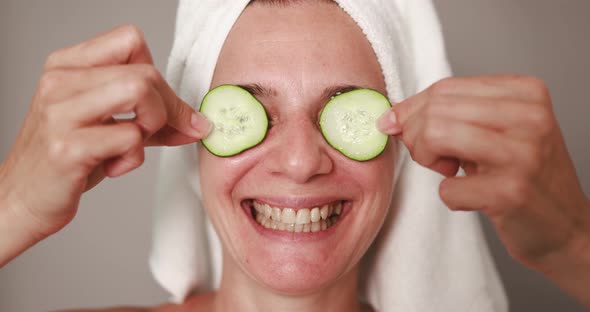 Mature caucasian woman having fun holding cucumbers on her eyes - Skin care therapy alt