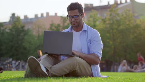 Young Indian Businessman Using Laptop Computer on Green Grass in Park alt
