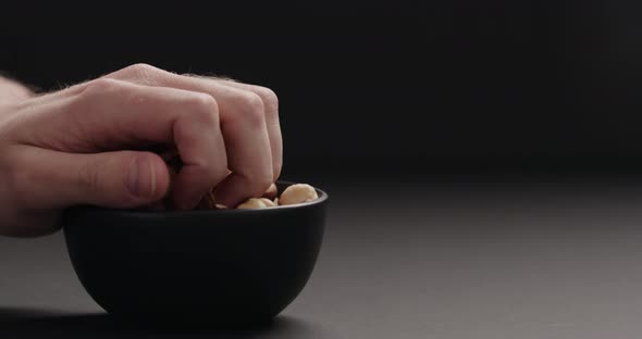 Slow Motion Man Hand Take Roasted Hazelnuts From Black Bowl on Black Background alt