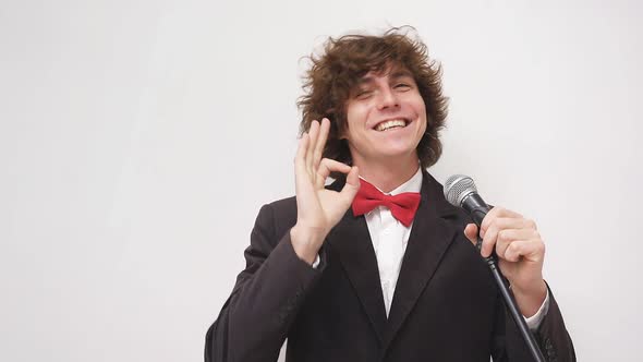 A Man in a Suit with a Microphone Demonstrating a GOOD Gesture and Smiling a Presentation or Speech alt