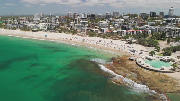 Aerial drone footage of ocean waves on a busy Kings beach, Caloundra, Australia alt
