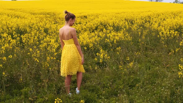 Pretty Model Spinning on a Field of Canola Flowers While Holding Her Mini Dress alt