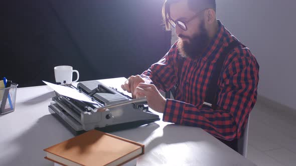 Writer's Day Concept. Young Male Writer in a Dark Room Typing on a Typewriter alt